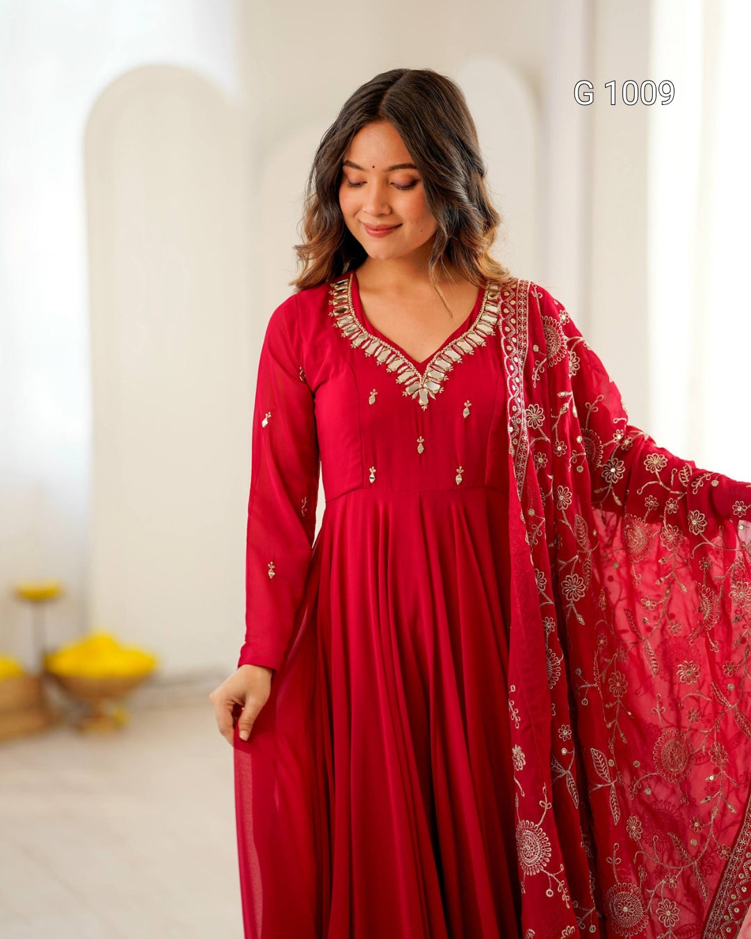 A woman wearing a red long-sleeve kurta with ornate gold embroidery around the neckline and matching red embroidered dupatta, standing in a bright indoor setting.