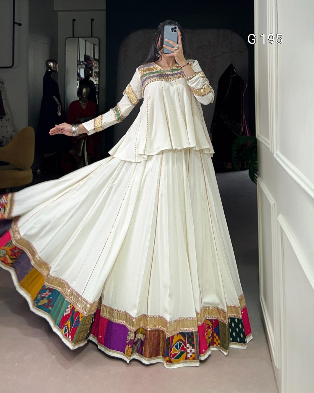 White traditional outfit with colorful border being modeled indoors.