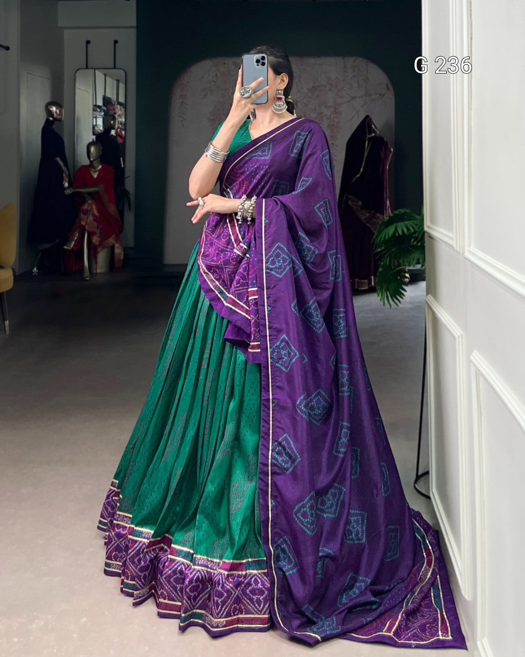 Woman wearing a green and purple saree in a room with mirrors and furniture.