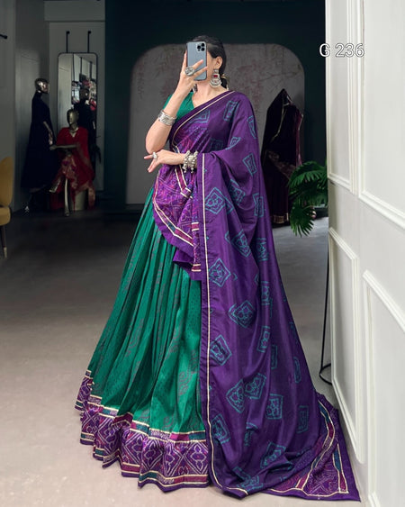 Woman wearing a green and purple saree in a room with mirrors and furniture.