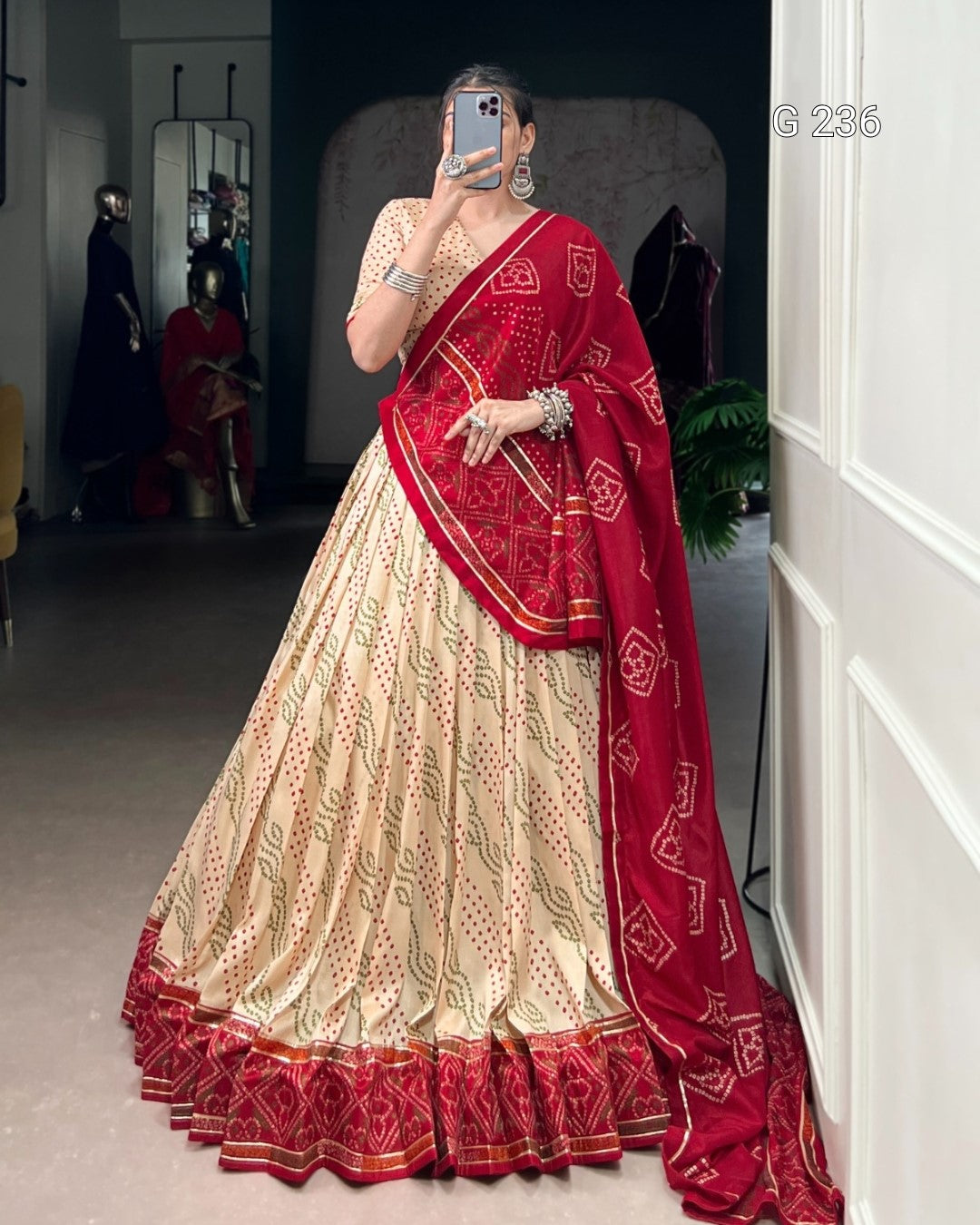 Person wearing a traditional outfit with a red and cream saree in an indoor setting.