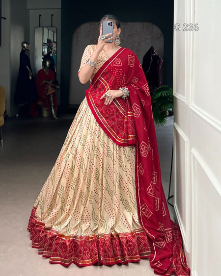 Person wearing a traditional outfit with a red and cream saree in an indoor setting.