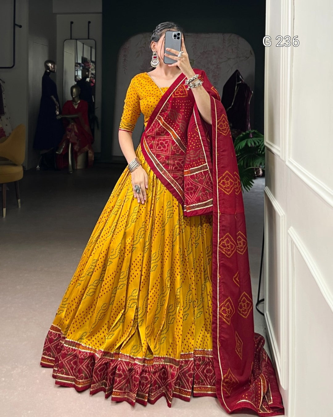 Woman wearing a yellow and red saree taking a mirror selfie.
