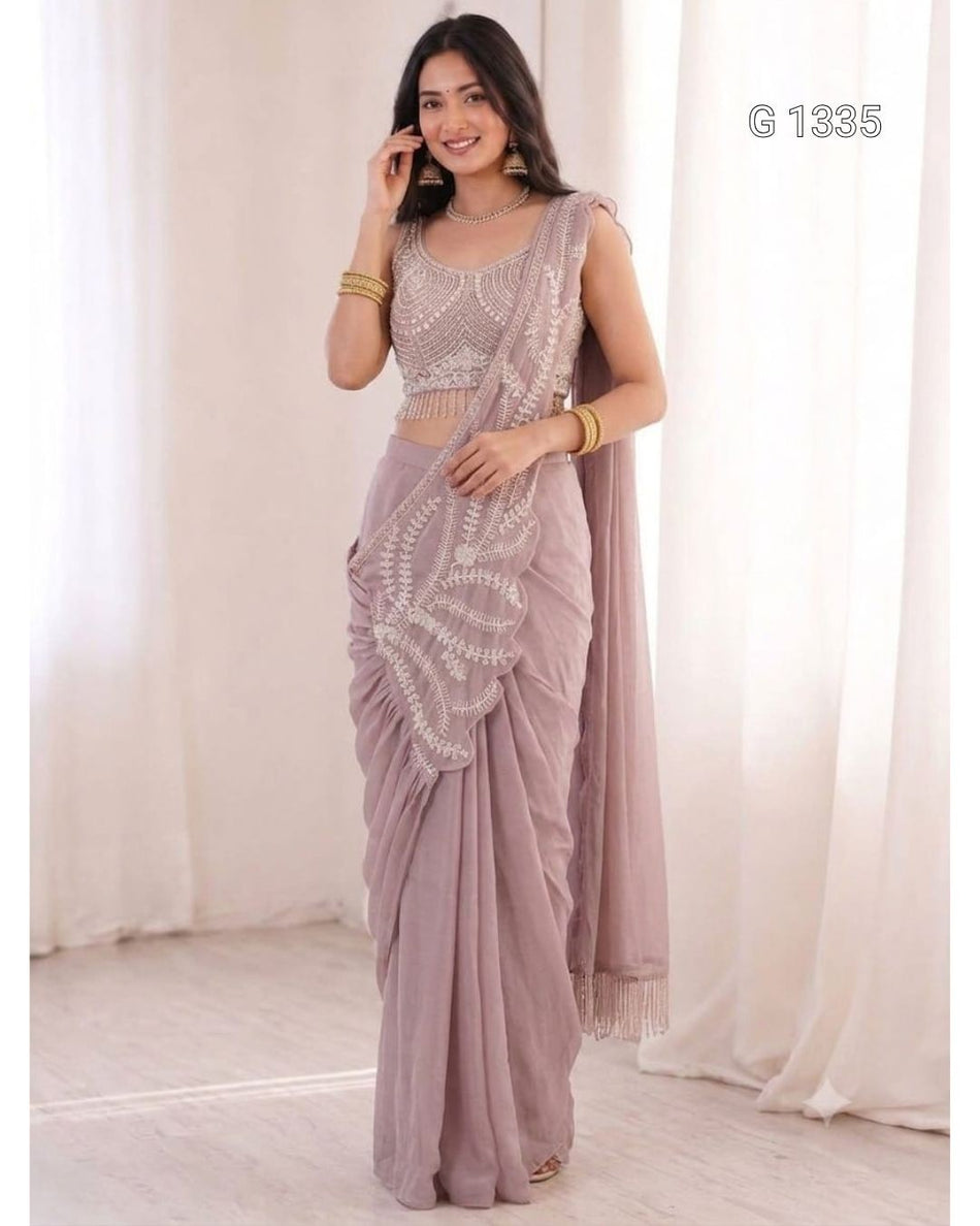 A woman wearing an elegant mauve saree with intricate white embroidered detailing and a matching sleeveless blouse.