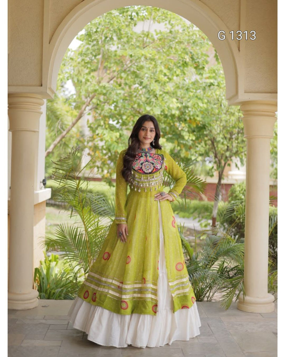 A woman models a lime green Anarkali gown with a white underskirt, standing under a stone archway with green garden foliage in the background. The dress features colorful embroidery on the chest and circular motifs on the skirt.