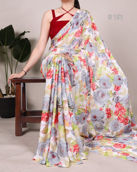 Woman wearing a floral saree with a red blouse, sitting on a wooden stool.