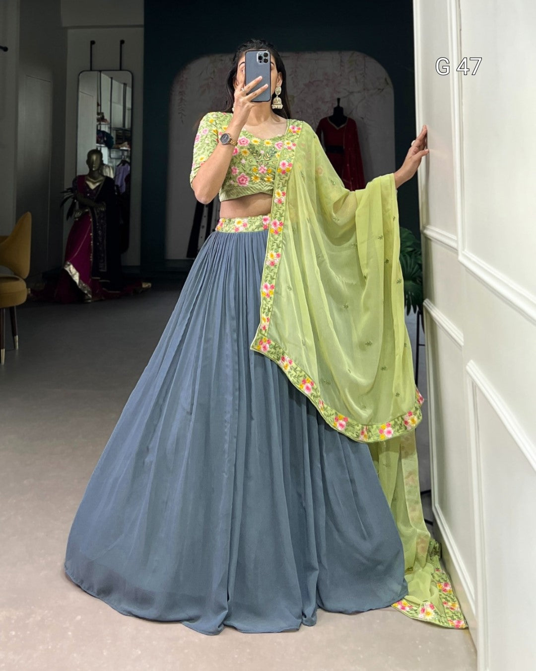 Person wearing a traditional outfit with a green blouse and blue skirt, standing in a room.