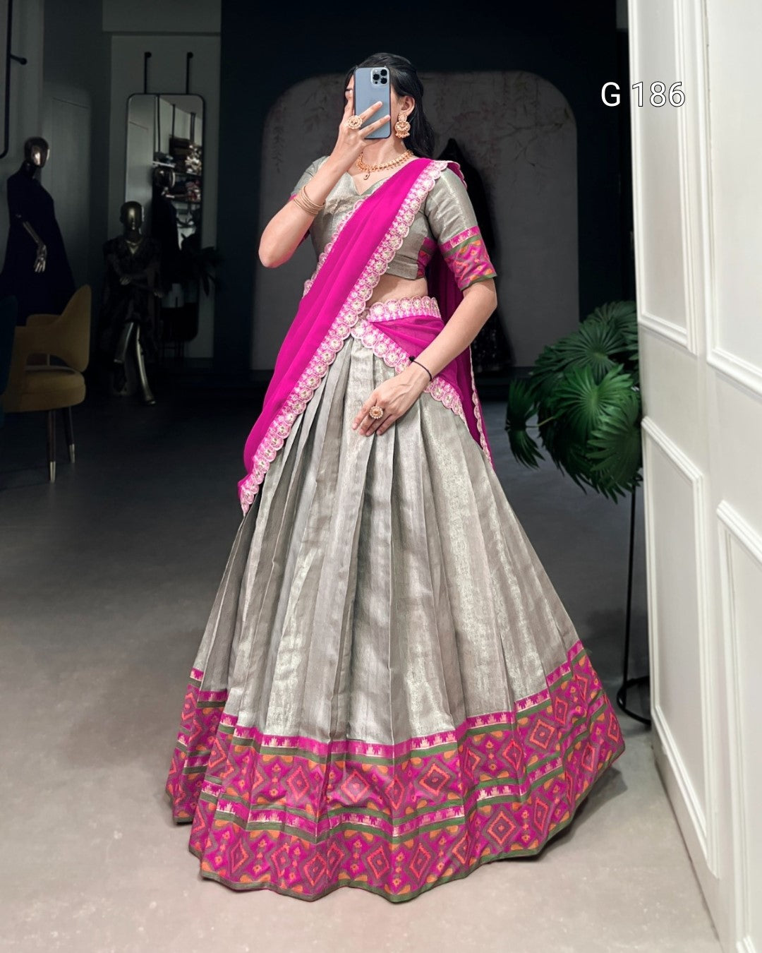 Woman wearing a traditional outfit with a pink and gray saree in a room.