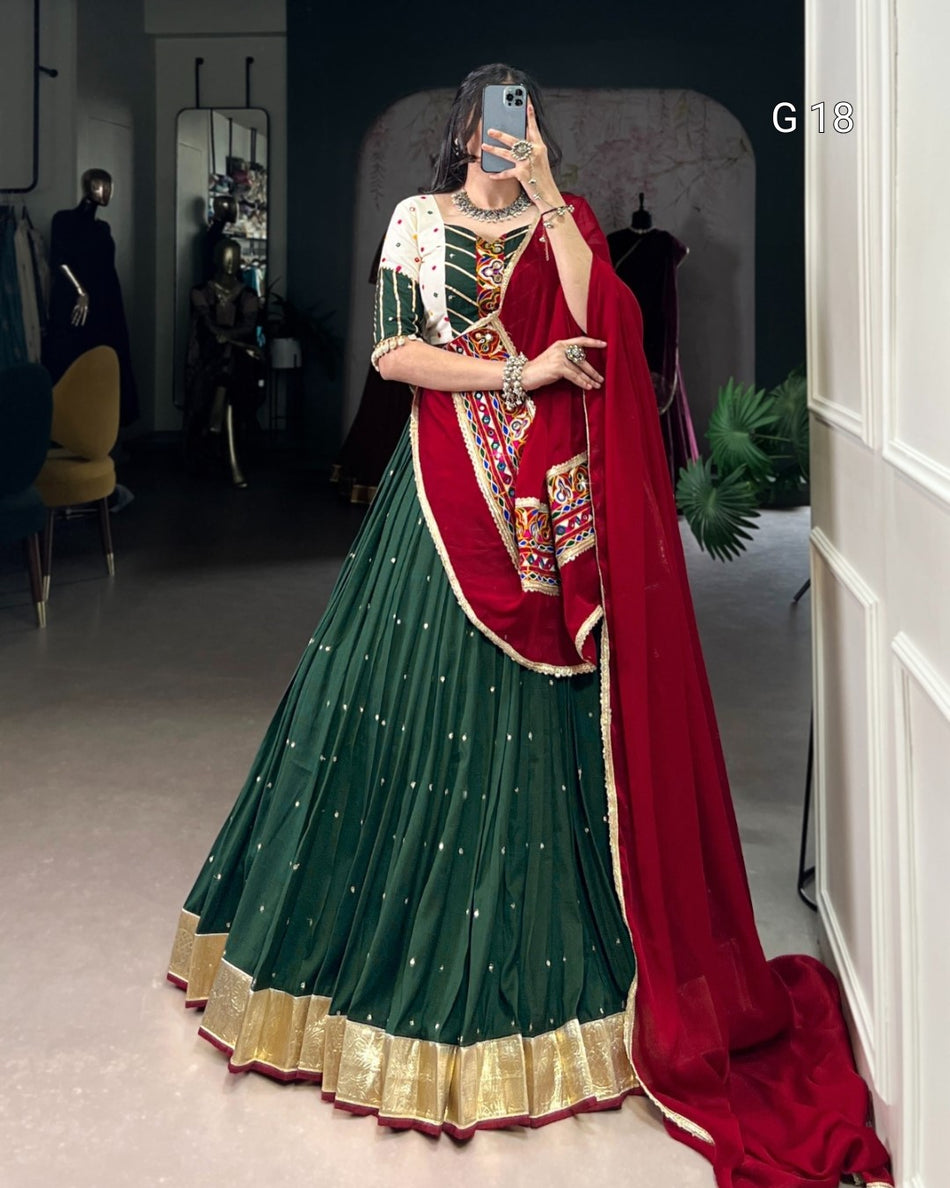 Person wearing a green and red traditional outfit with gold details, standing in a room.