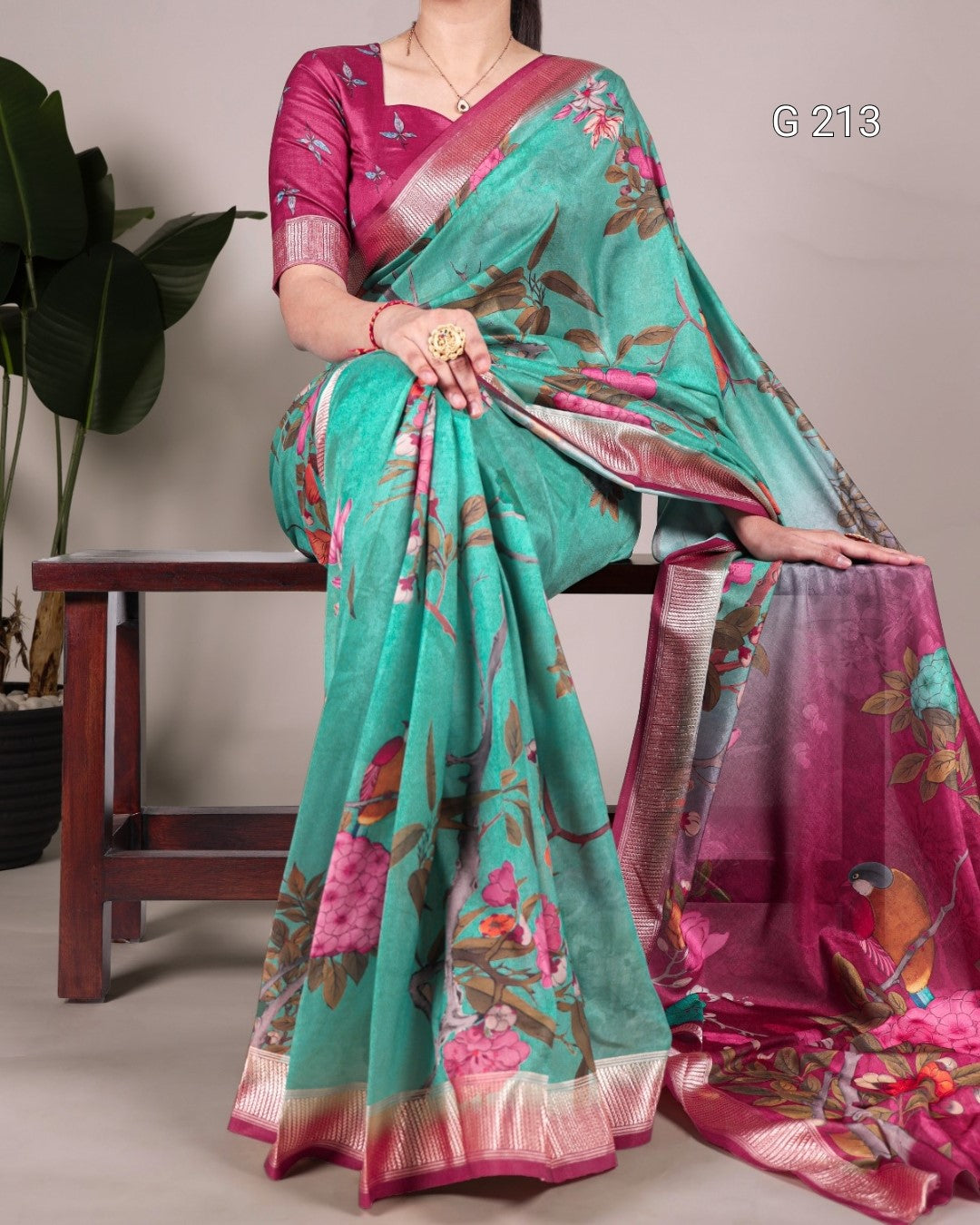 Woman wearing a teal and pink saree with floral patterns, sitting on a chair.