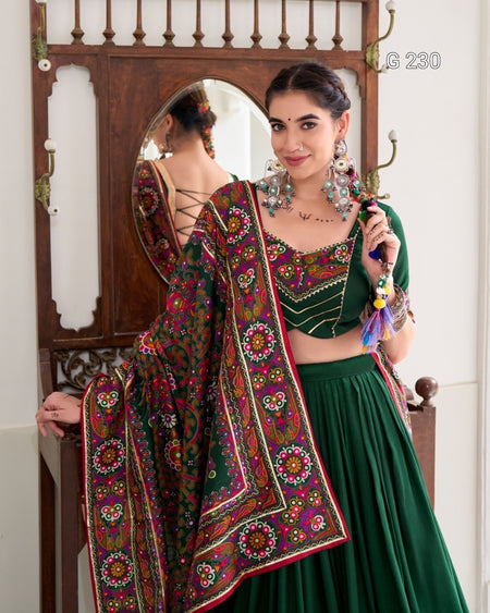 Woman in traditional green and multicolored outfit with jewelry, standing in front of a mirror.