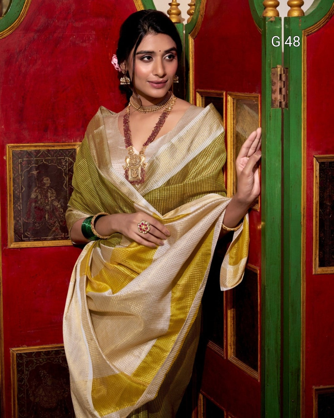 Woman in a yellow and white saree with jewelry against a red and gold background