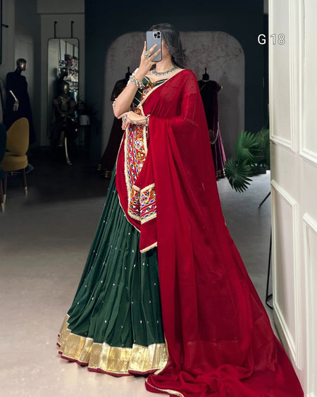 Person wearing a green and red saree with a patterned blouse in a room.