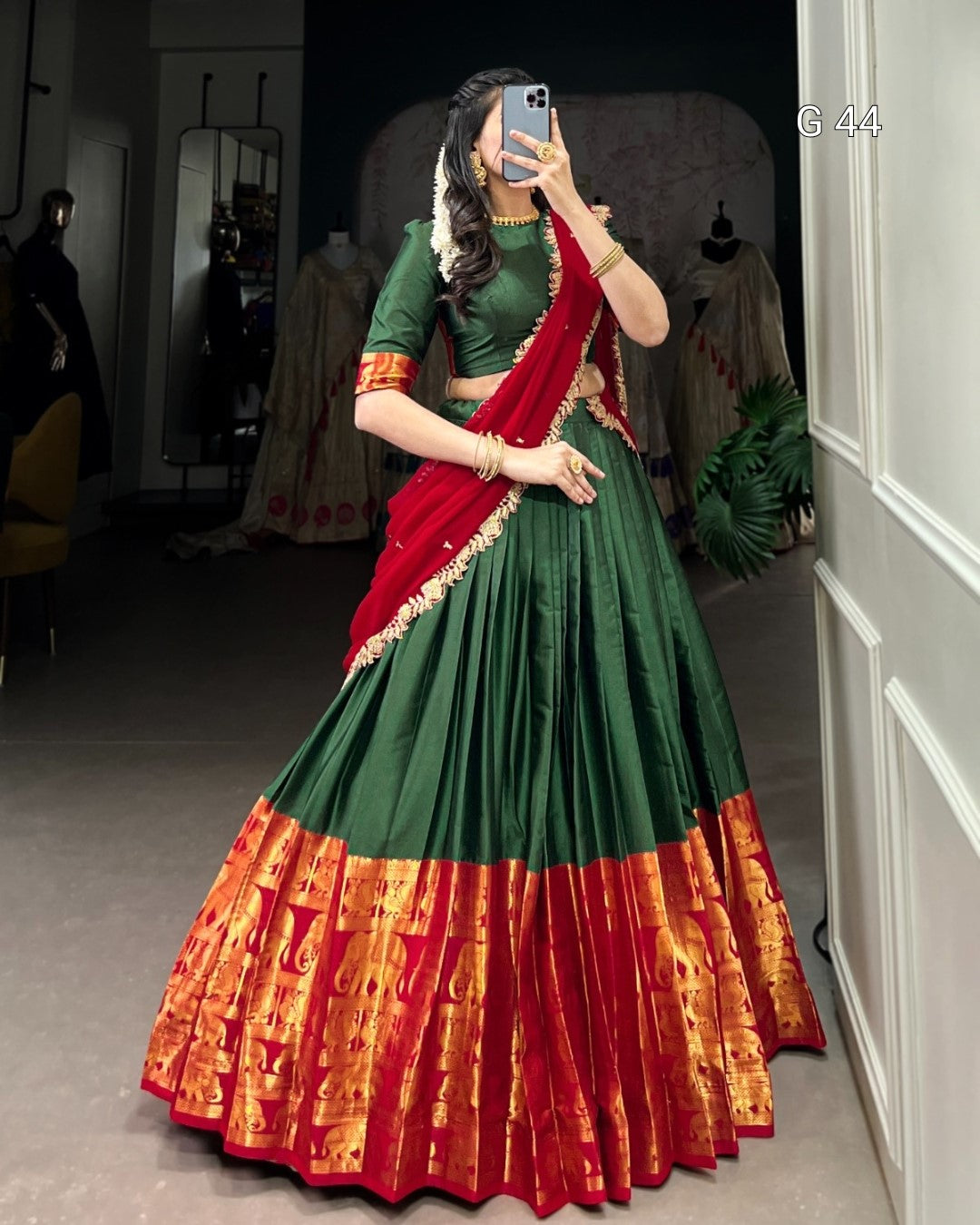 Person wearing a green and red traditional outfit with a patterned skirt, standing in a room.