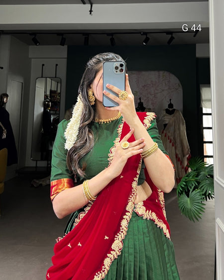 Person wearing a green and red saree with gold accents, taking a mirror selfie.