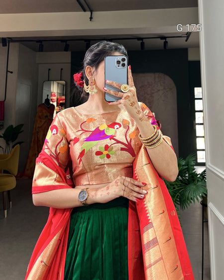 Woman in traditional outfit with colorful blouse and green saree, holding phone.