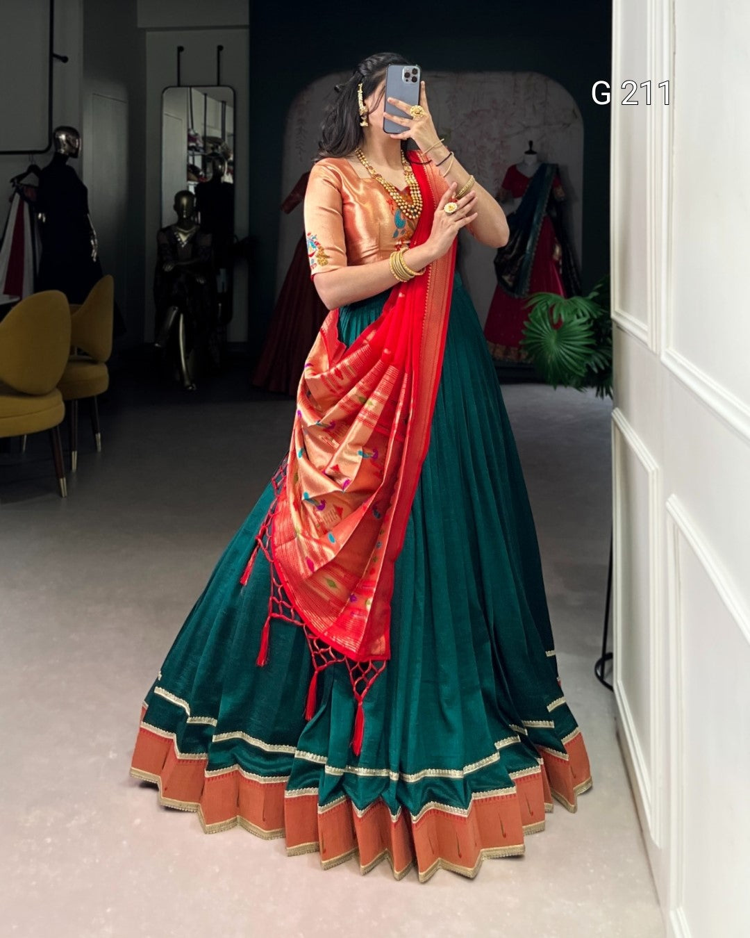 Woman wearing a traditional saree with a red blouse and green skirt in a room.
