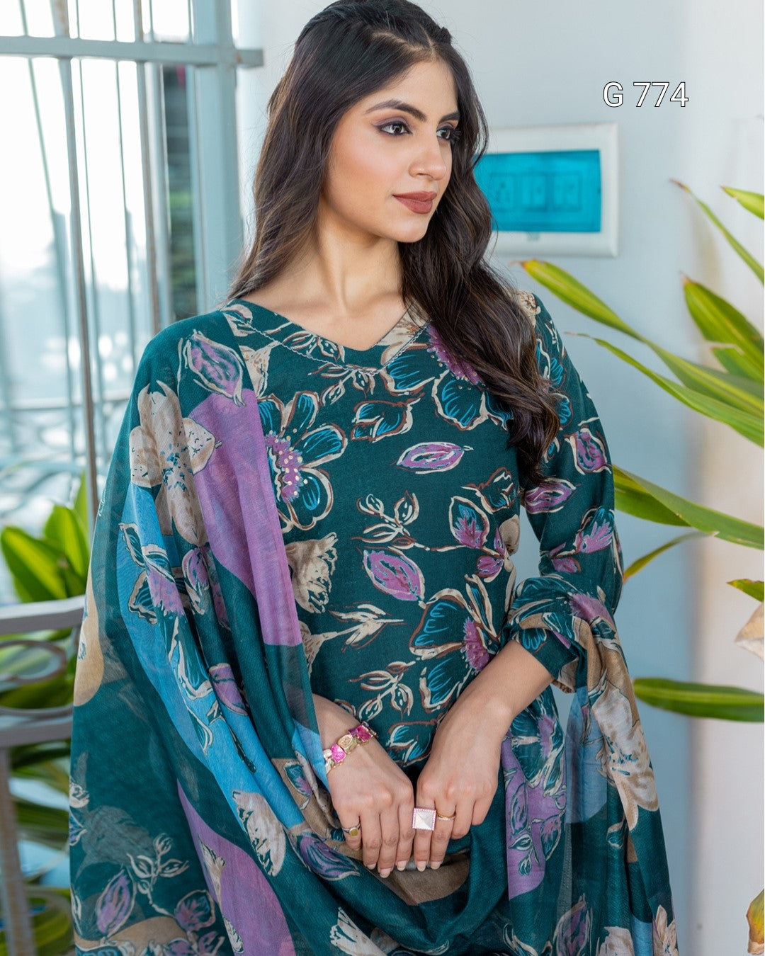 Woman wearing a green floral dress with a purple scarf in an indoor setting.