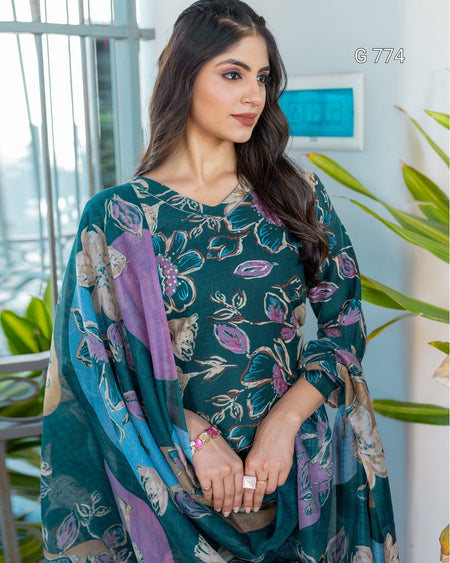 Woman wearing a green floral dress with a purple scarf in an indoor setting.