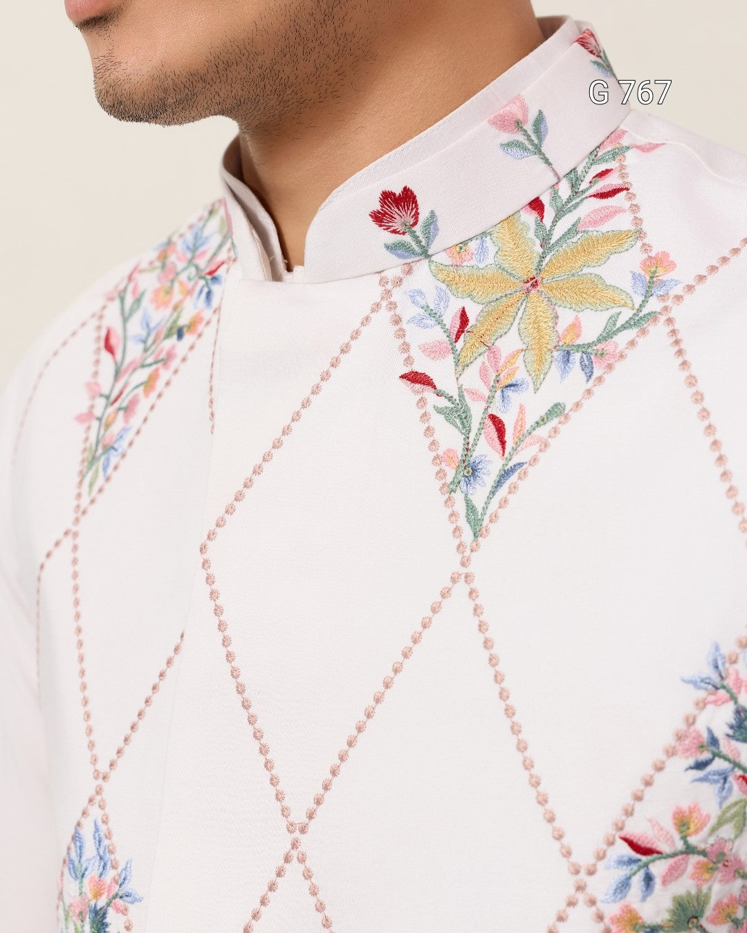 Close-up of a white embroidered shirt with colorful floral patterns on a beige background.