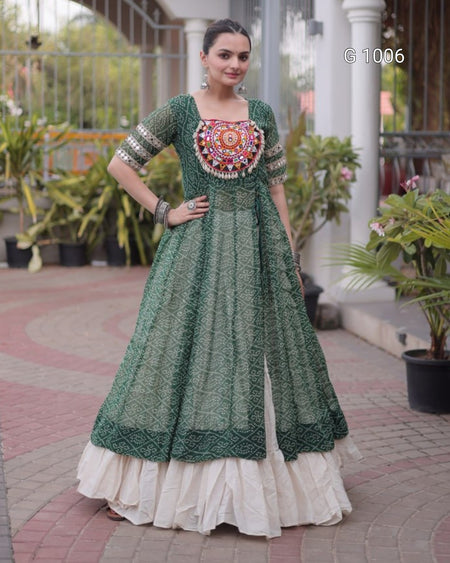A woman models a green printed Anarkali gown with a heavily embellished mandarin-styled bodice and a layered cream ruffled underskirt, set against a residential outdoor backdrop with potted plants.