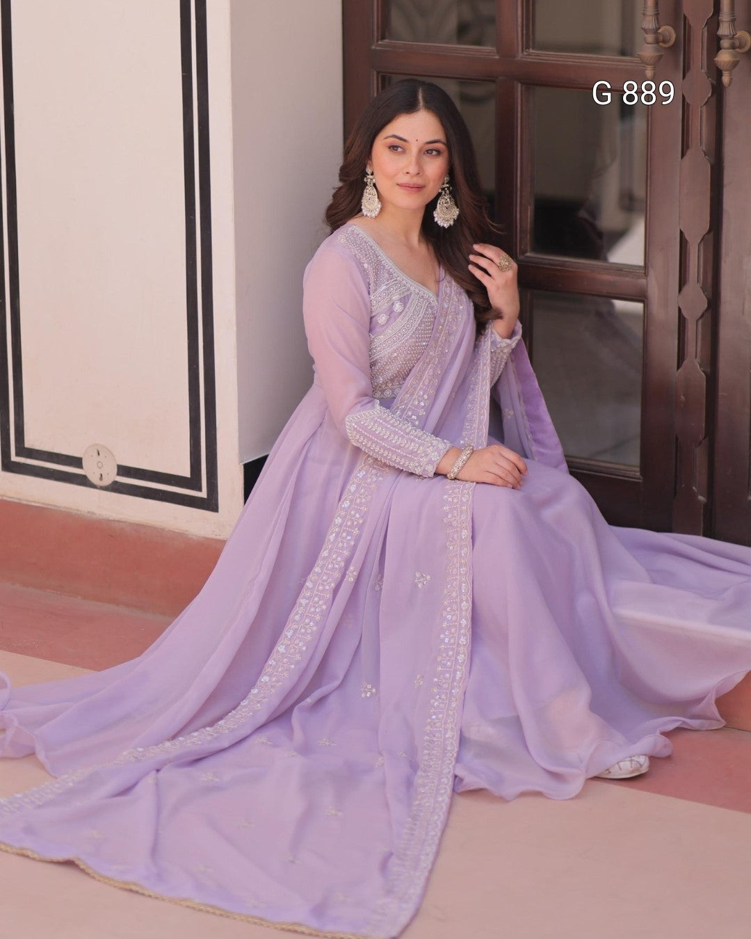 Woman in a lavender traditional outfit with intricate designs, sitting on a step.