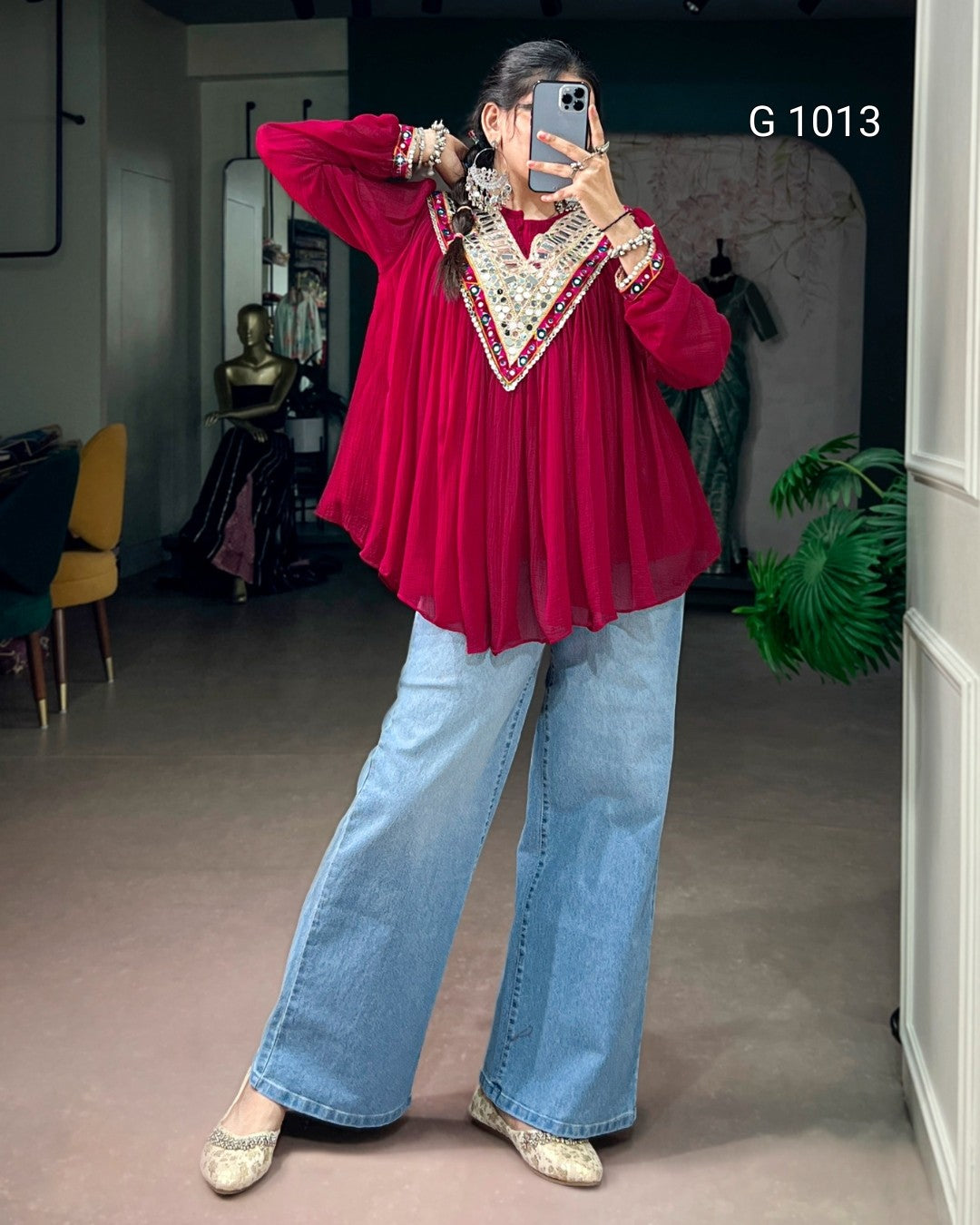 A woman takes a mirror selfie in a boutique showing a red long-sleeve blouse with a large beige and red embroidered V-neck panel, paired with wide-leg light blue jeans and beige lace-up flats. The text 'G 1013' is visible in the top right corner.