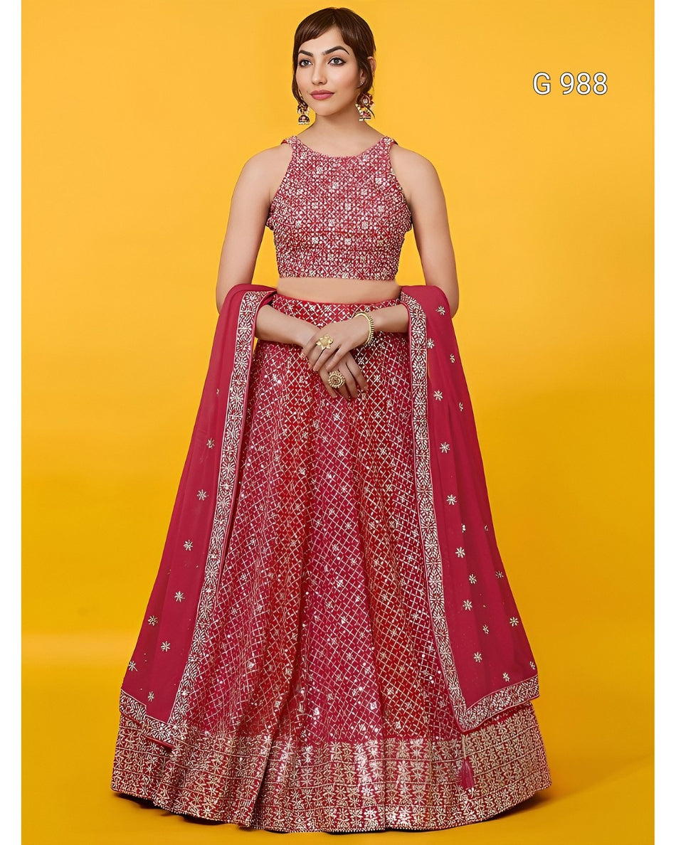 A woman models a traditional Indian lehenga choli set in a vibrant magenta pink with intricate gold and silver embroidery, set against a solid yellow studio background.