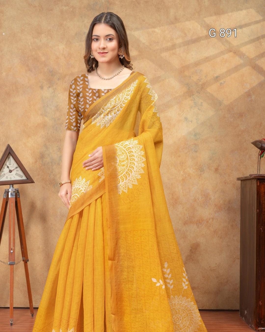 Woman wearing a yellow saree with white embroidery against a brown background
