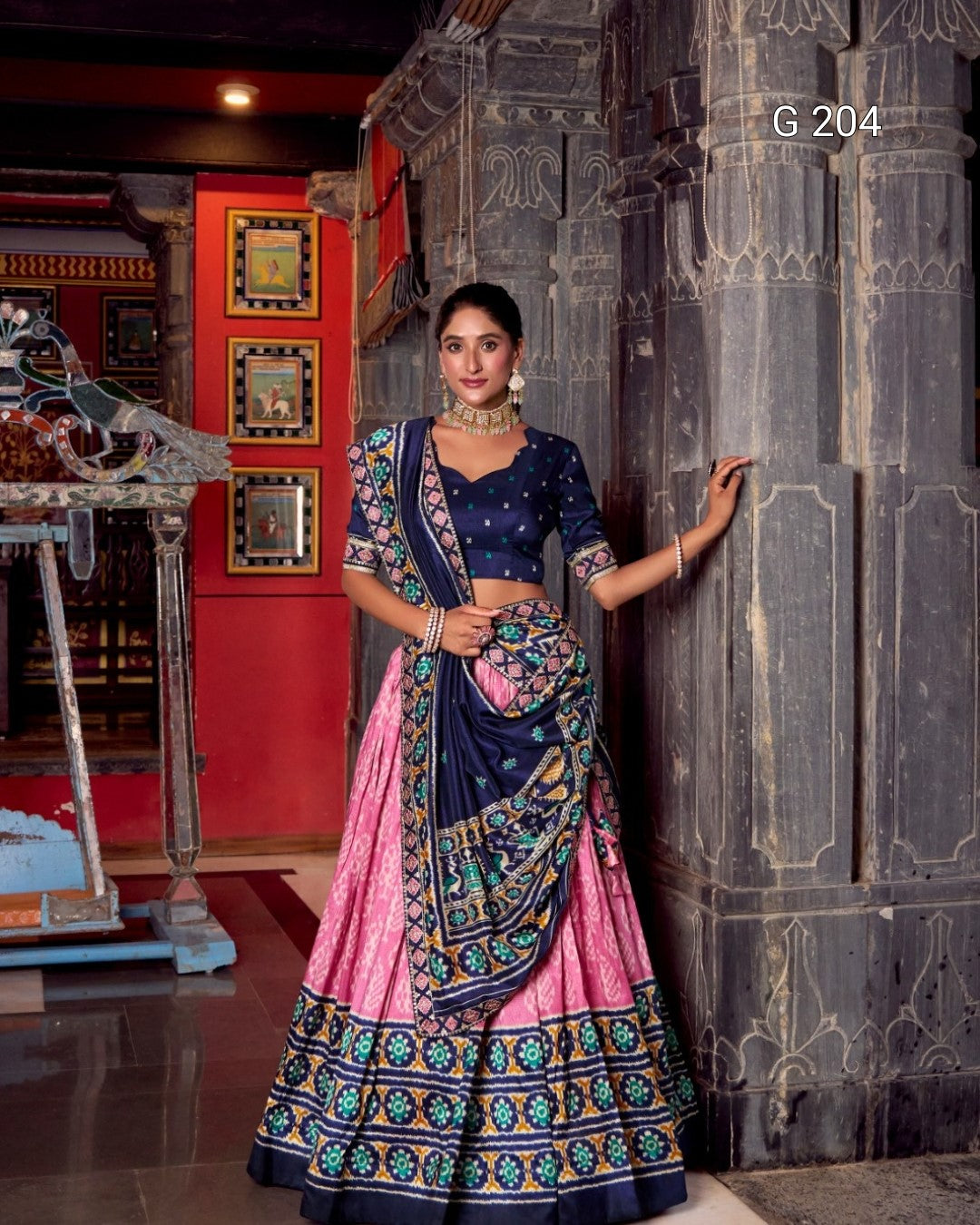 Woman in a traditional outfit standing against a decorative wall.