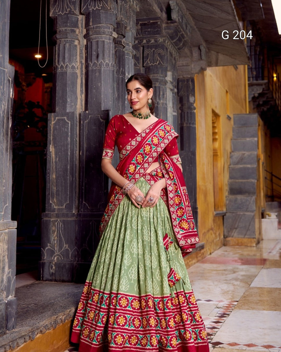 Woman in a traditional red and green saree with floral patterns standing in an architectural setting.