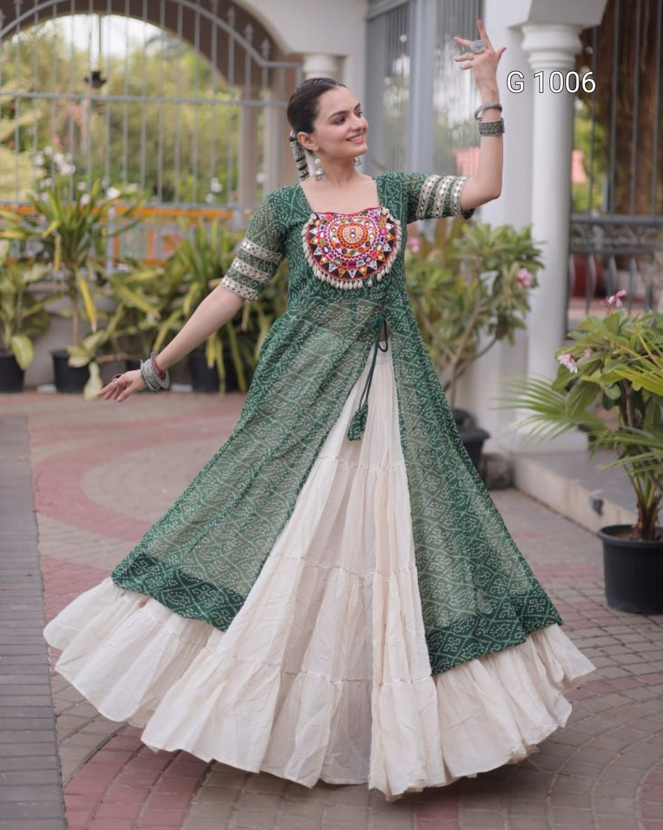 A woman modeling a traditional Indian outfit featuring a dark green embroidered kurta with a highly detailed, colorful embroidered yoke and a tiered cream-colored skirt, set against an outdoor patio background with potted plants.