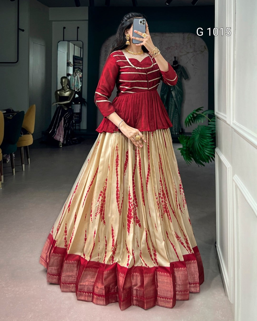 A woman takes a mirror selfie in an indoor boutique setting wearing a traditional Indian outfit consisting of a deep red peplum top and a voluminous beige skirt with red tie-dye patterns and a red border. The text 'G 1015' is visible in the top right corner.