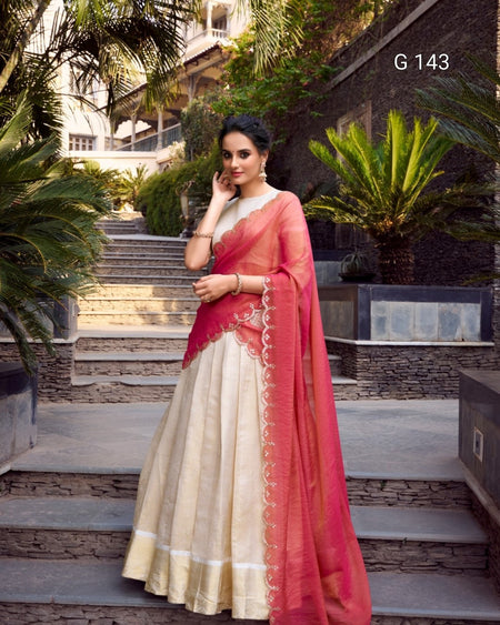 Woman in a pink and beige saree standing outdoors with plants and steps in the background
