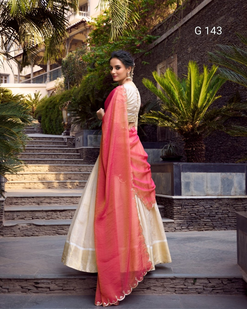 Woman in a pink and white saree standing outdoors with greenery and steps in the background