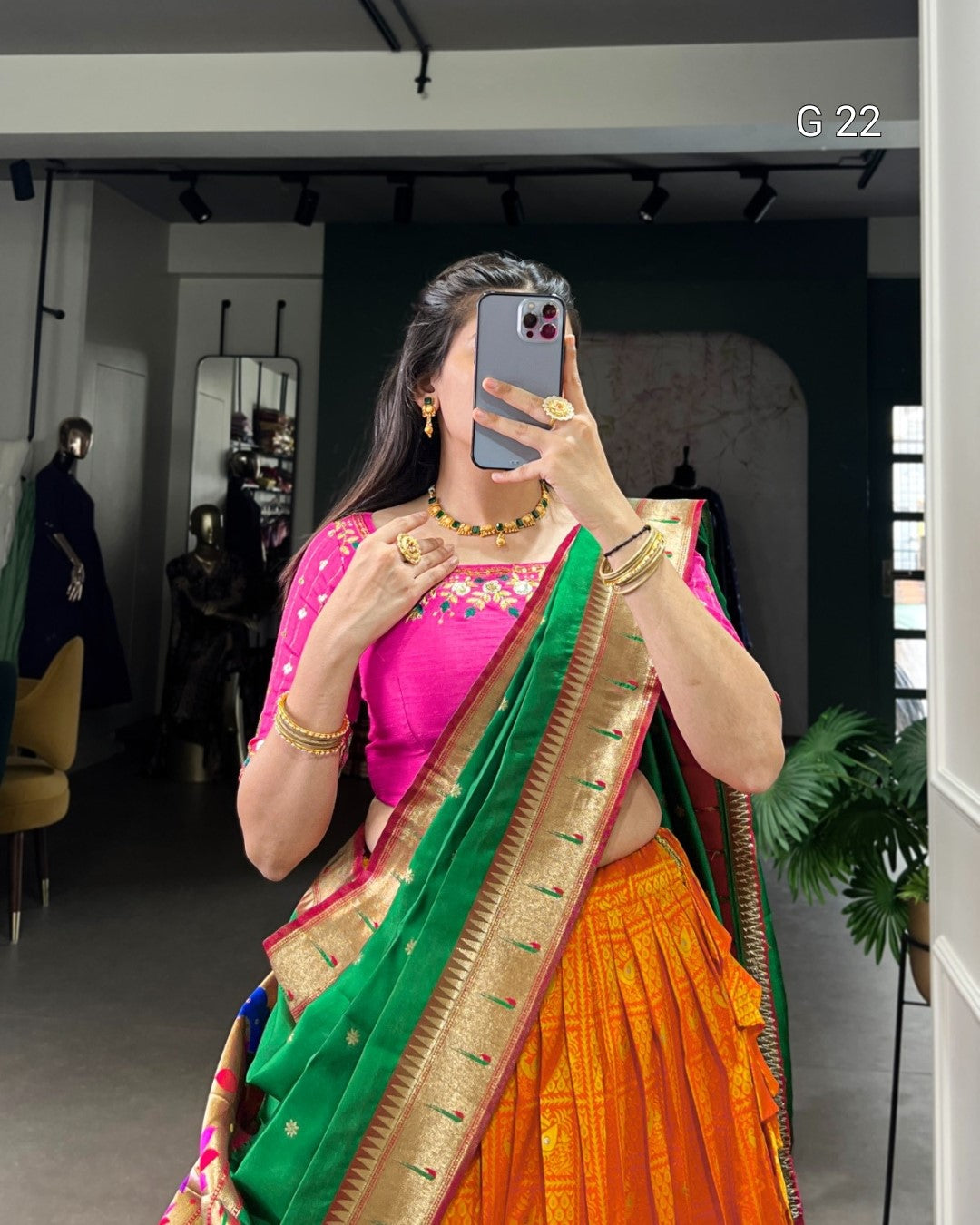 Woman taking a mirror selfie wearing a colorful saree in an indoor setting.