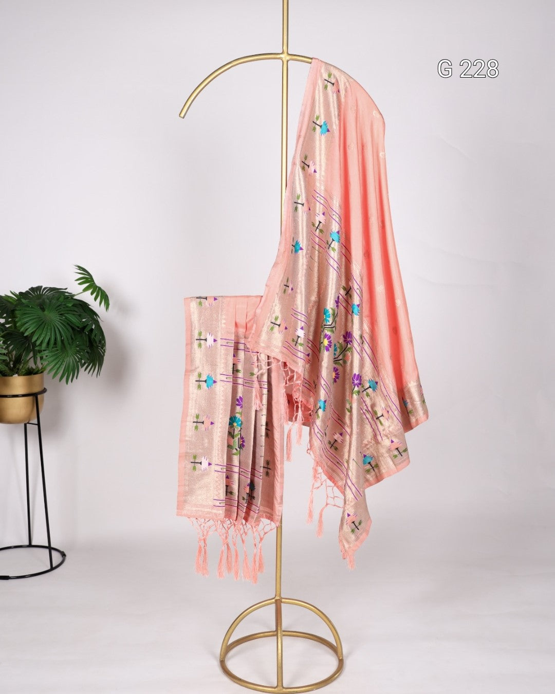 Pink scarf with floral patterns on a gold stand against a white background