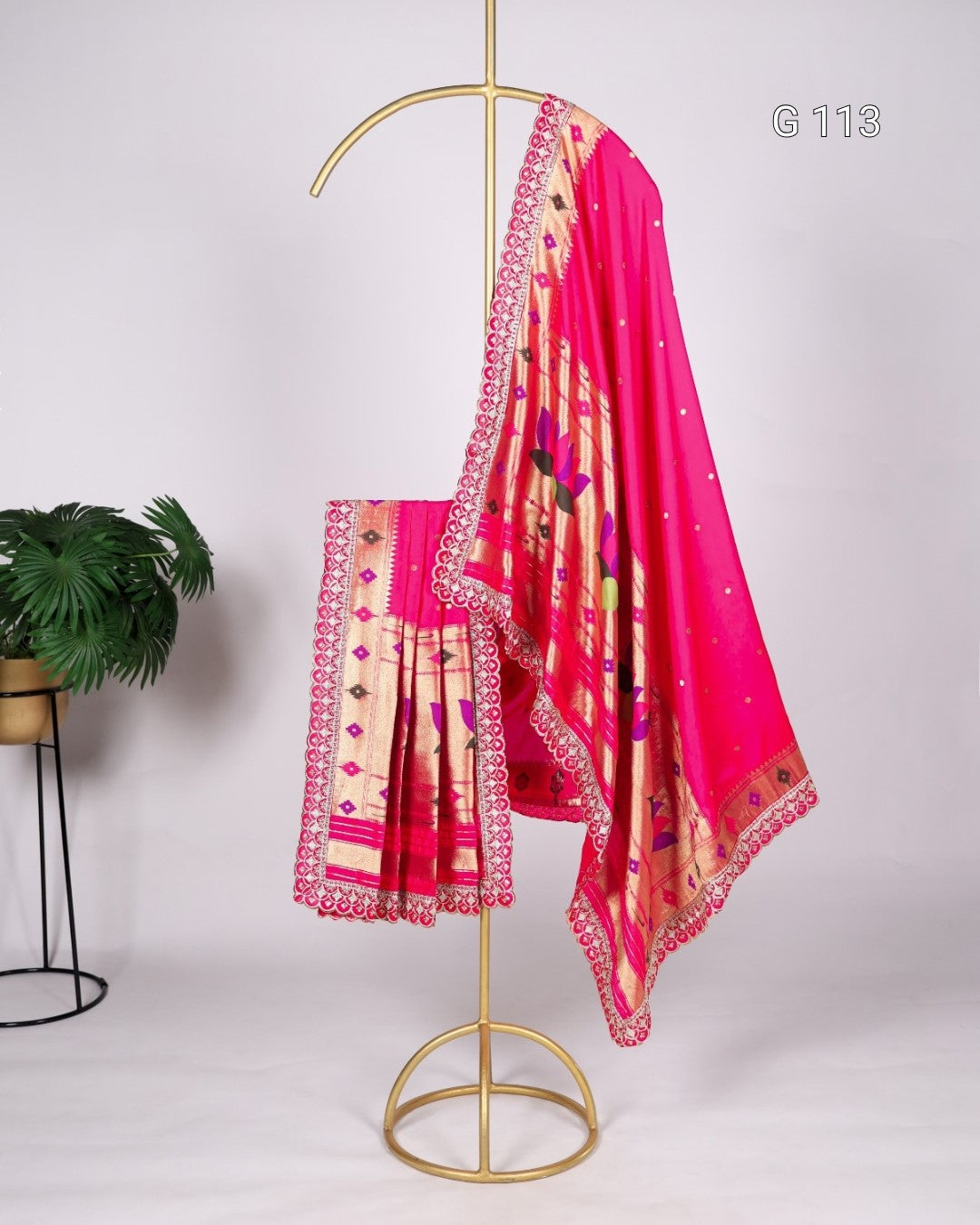 Pink saree with floral patterns on a gold stand against a white background