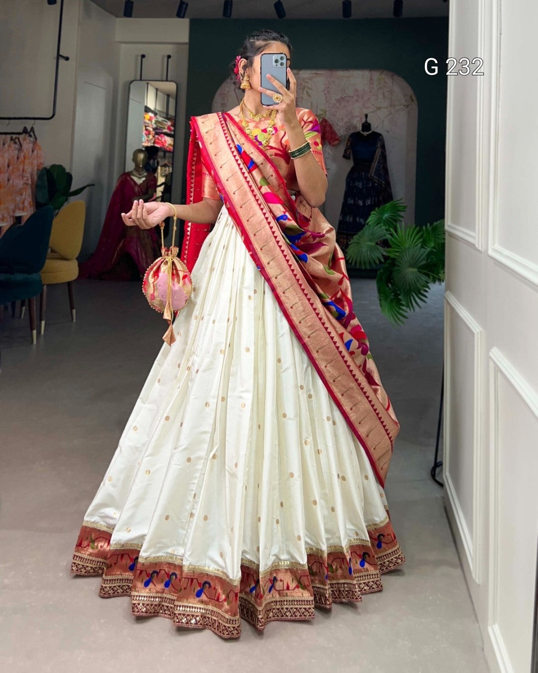 Woman wearing a traditional white saree with red and gold border in a room setting.