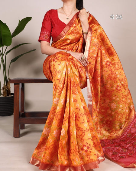 Woman wearing an orange saree with a red blouse, sitting on a wooden stool.