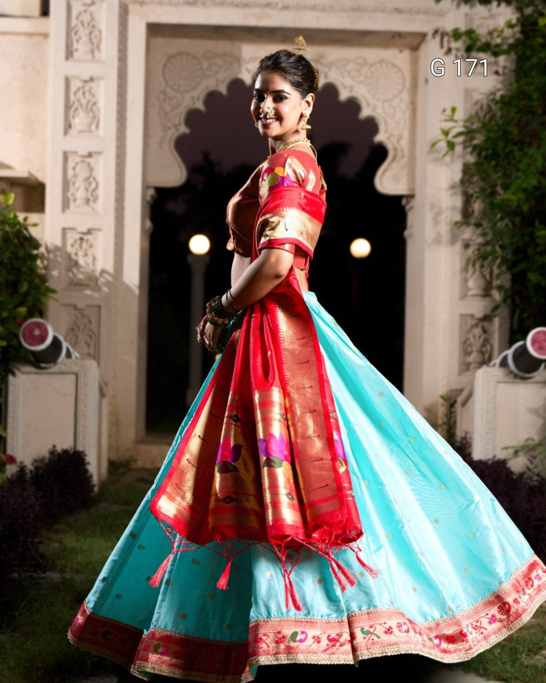 Woman wearing a traditional outfit with a red blouse and blue saree in an outdoor setting.