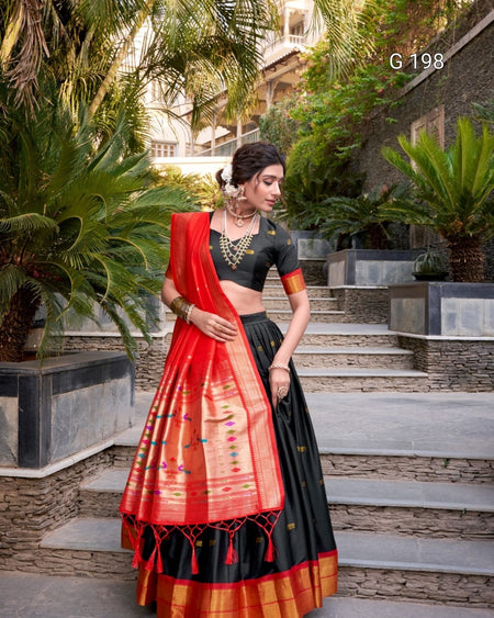 Woman in a red and black traditional outfit standing outdoors with greenery.