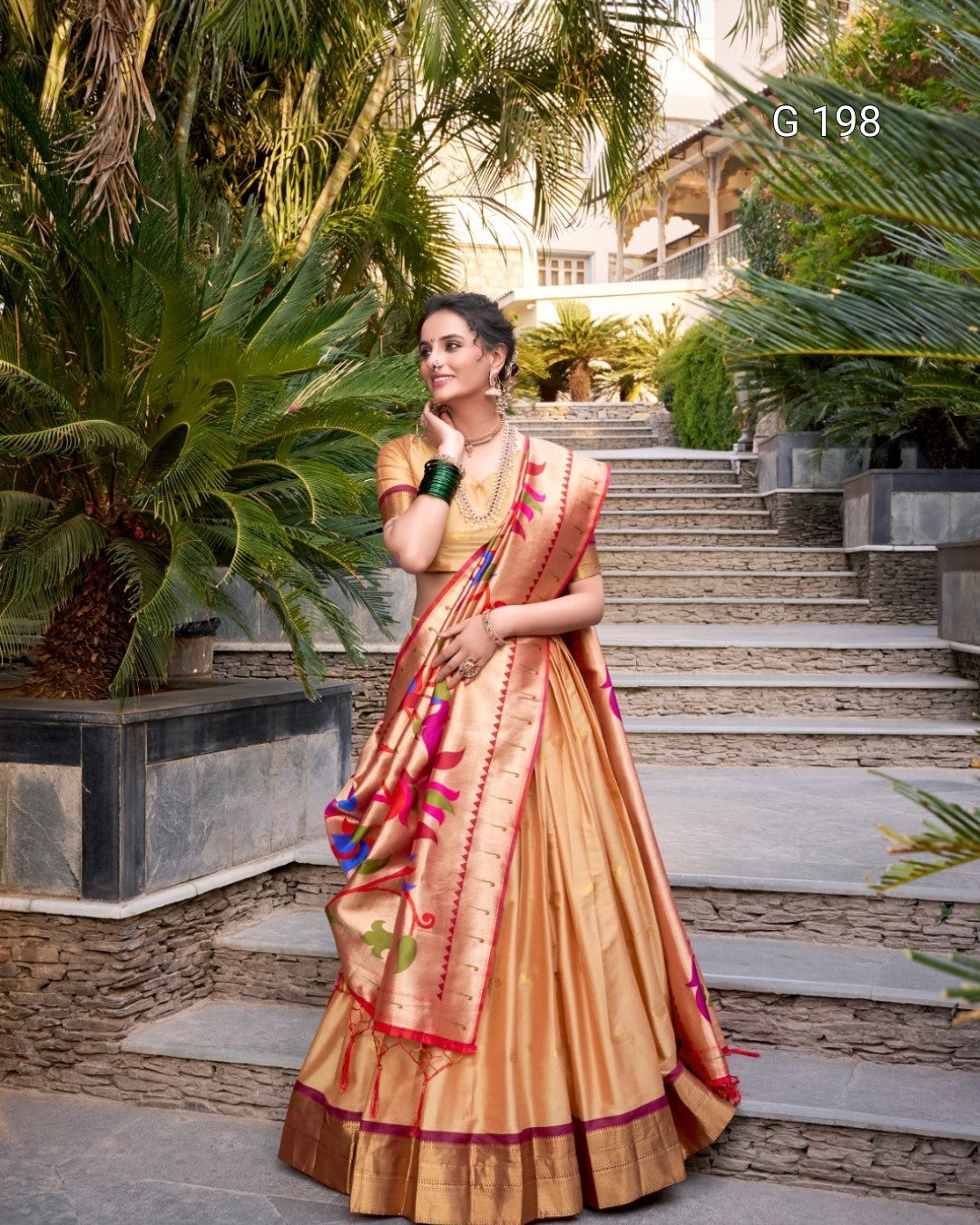 Woman in a traditional saree standing outdoors with greenery and steps in the background