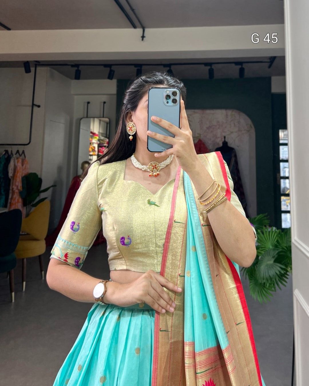Person wearing a traditional outfit with a green blouse and blue saree in a room.