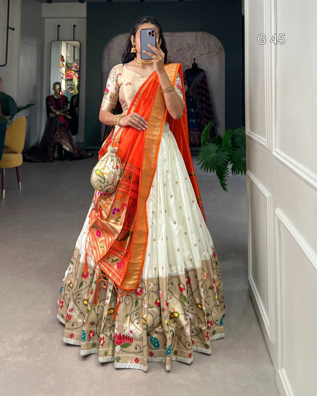 Woman wearing a traditional outfit with an orange dupatta in a room setting.
