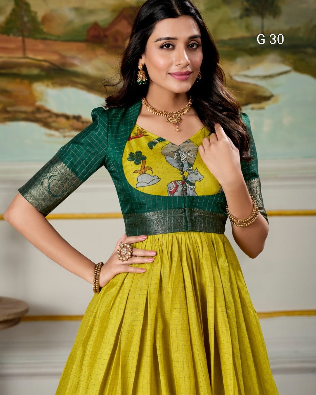 Woman wearing a green and yellow traditional outfit with floral patterns, standing in front of a scenic background.