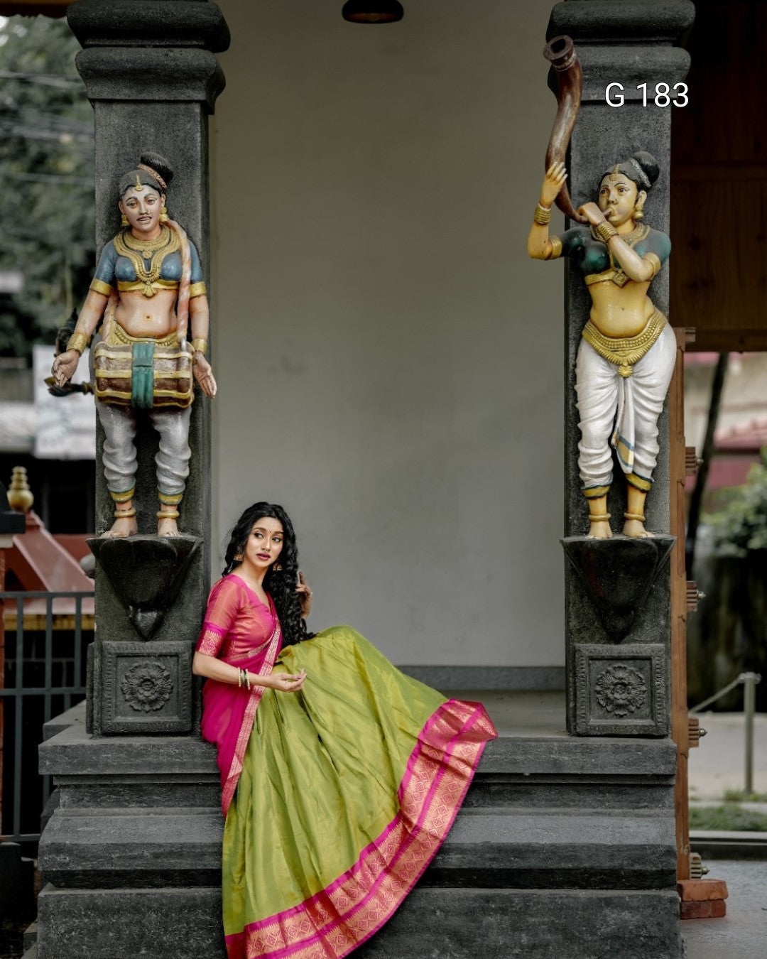 Woman in traditional attire sitting between two stone statues in a temple setting