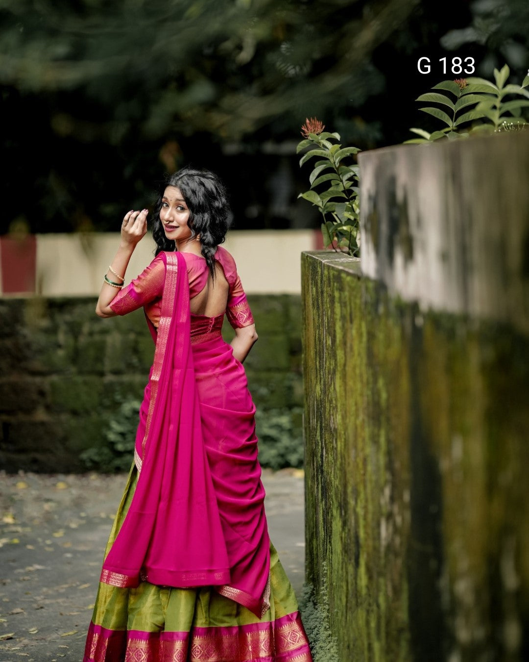 Woman in a pink saree with a green border standing outdoors.