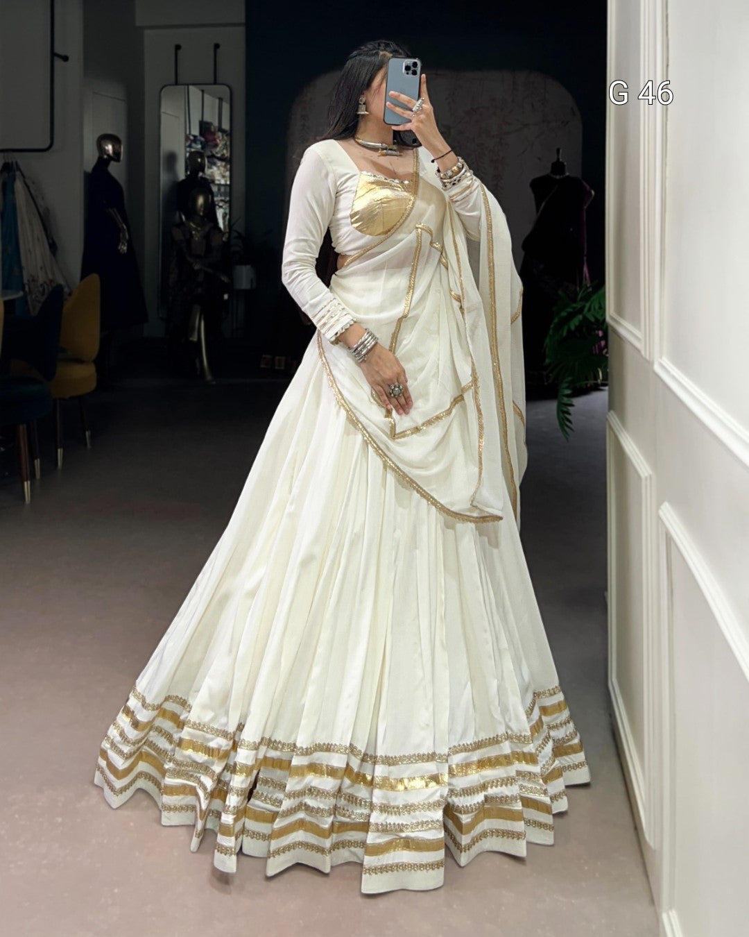 Person wearing a white saree with gold accents in a room.
