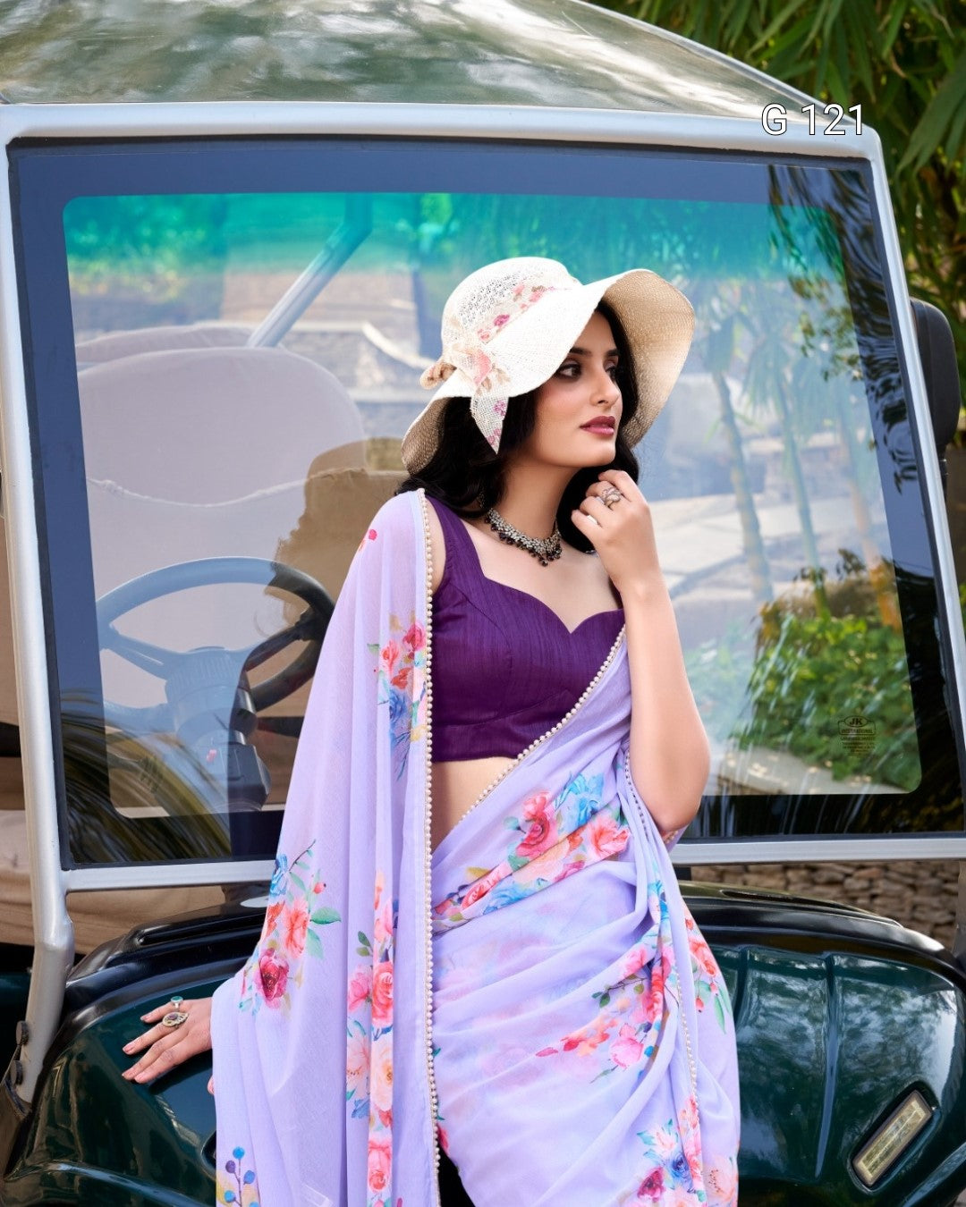 Woman in a colorful saree and hat standing next to a car